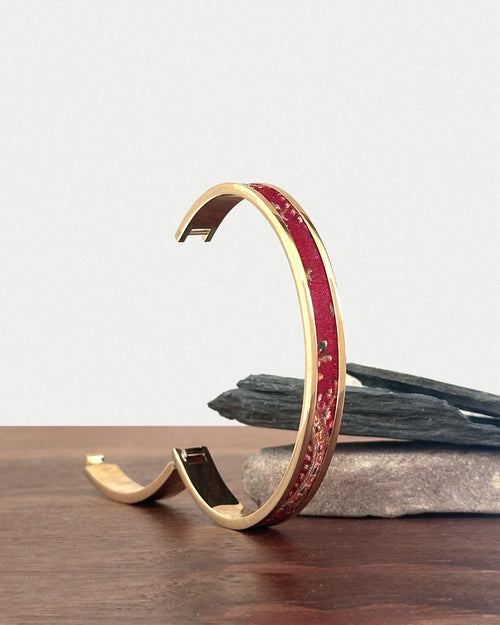 Gold bracelet with red accents on a wooden surface